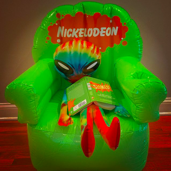 Inflatable alien sitting and holding a book in inflatable slime green colored chair with orange nickelodeon logo